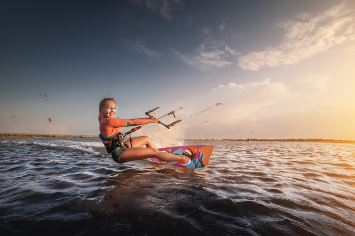 Water sports. The girl is engaged in kitesurfing with a kite in the sky on board in the blue sea, riding the waves with water splashes. Recreational activities, water sports, activities, hobbies and entertainment in the summer. kiteboarding.