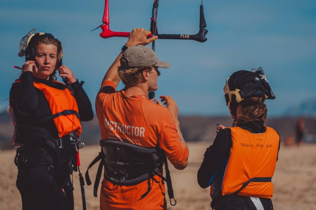 Kitesurfing instructor giving a beachside lesson to students in safety gear at Tarifa, Spain, during a kiteboarding training session